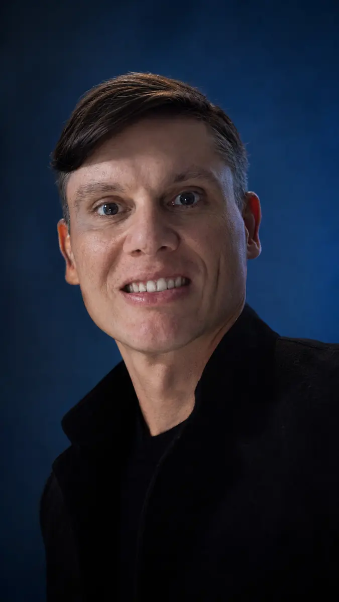 Retrato de Aldo Batista sorrindo, sobre fundo azul