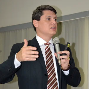 Aldo Batista palestrando de terno, com microfone